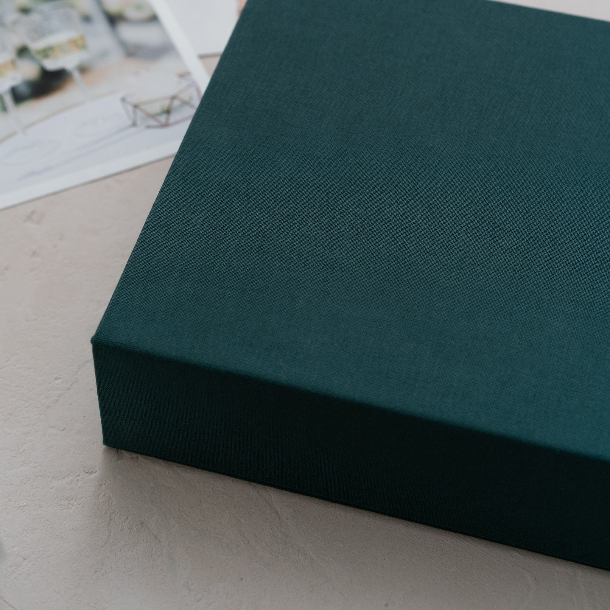 A dark green box rests on a white surface, with a blurred image of a bicycle visible in the background.