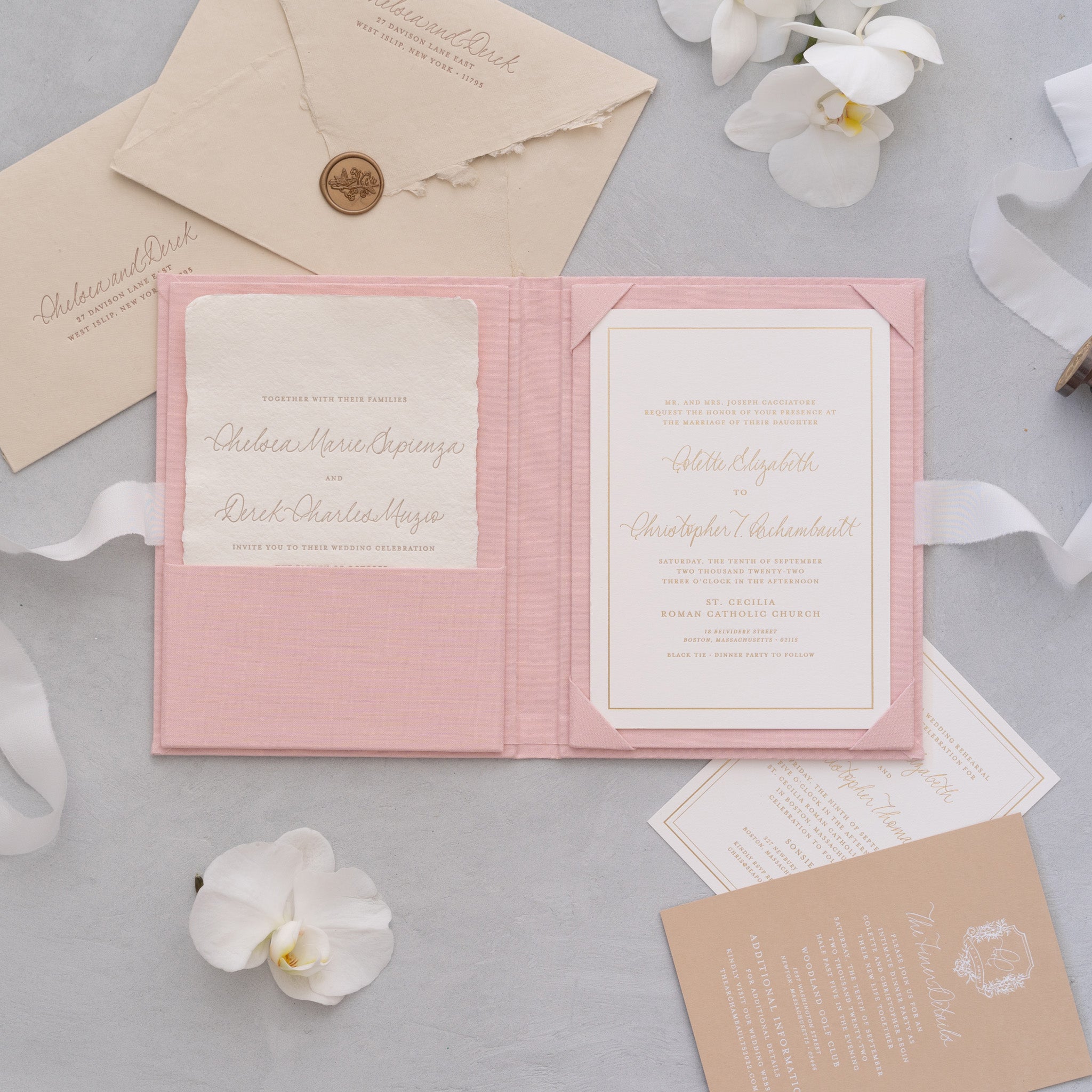 a pink wedding invitation card with a white flower, surrounded by other wedding-related items such as envelopes, a ribbon, and a card.