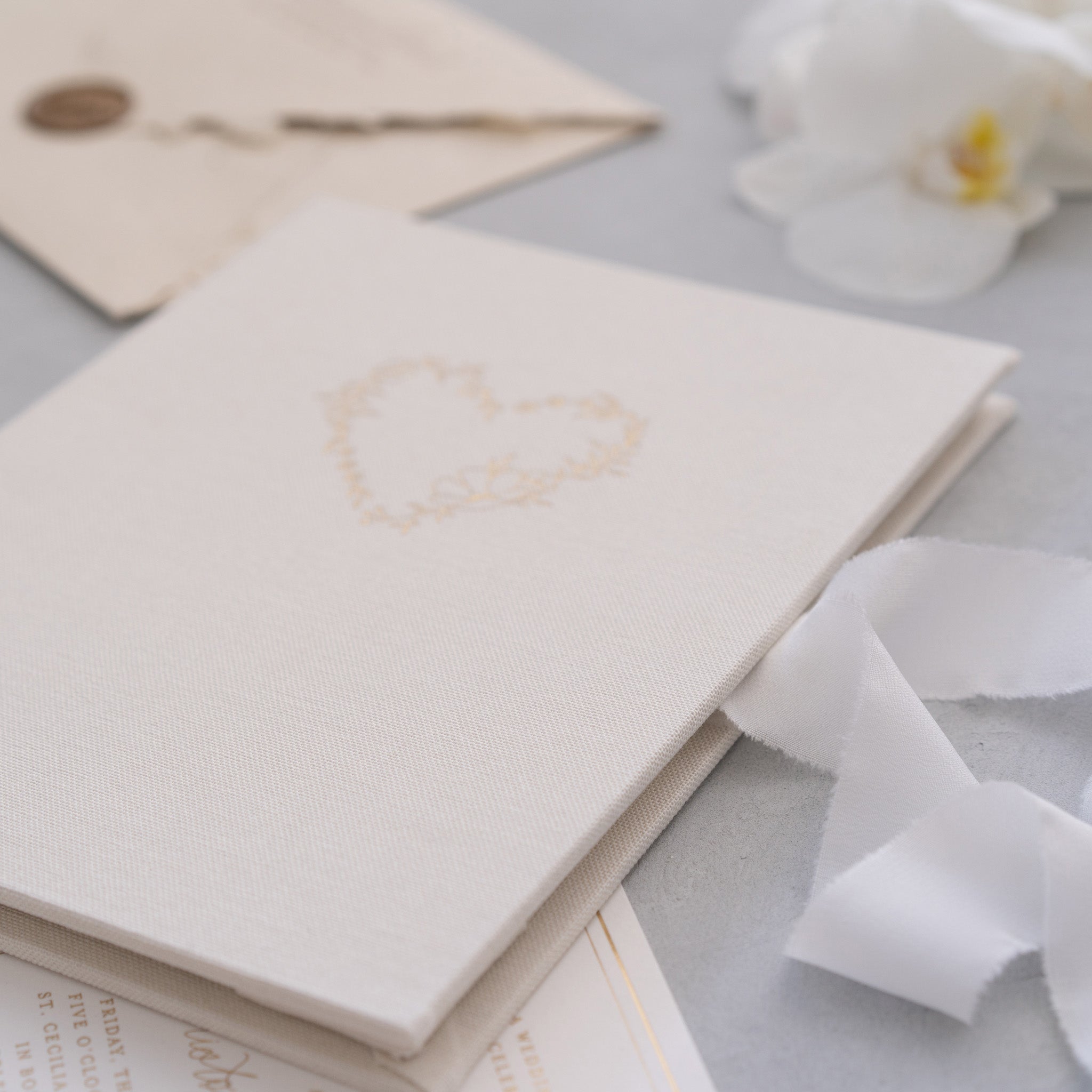 a close-up view of a white card with a heart design, placed on a surface with a white flower and some white ribbon.