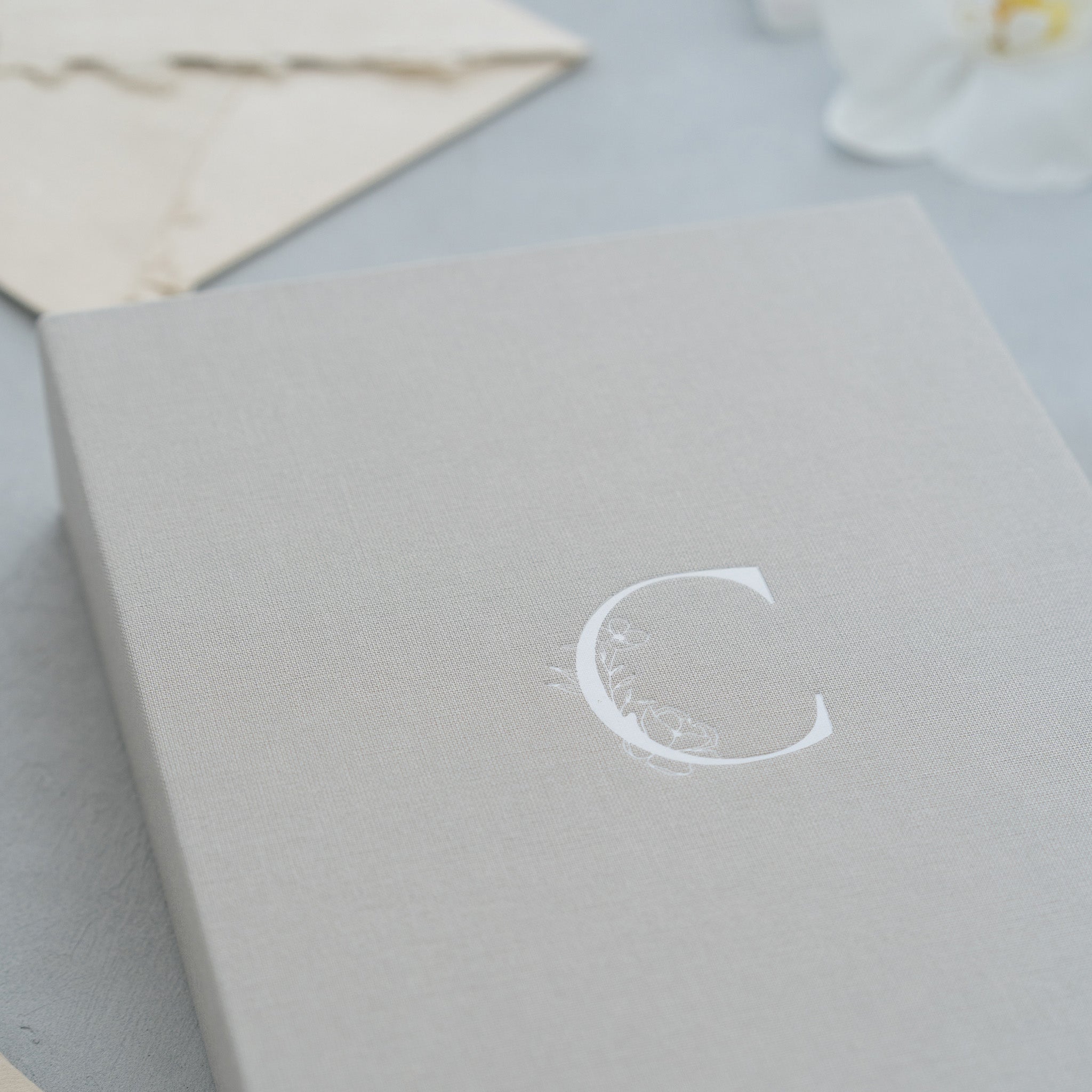 A close-up view of a gray box with a white letter 'C' printed on it, along with some white flowers in the background.
