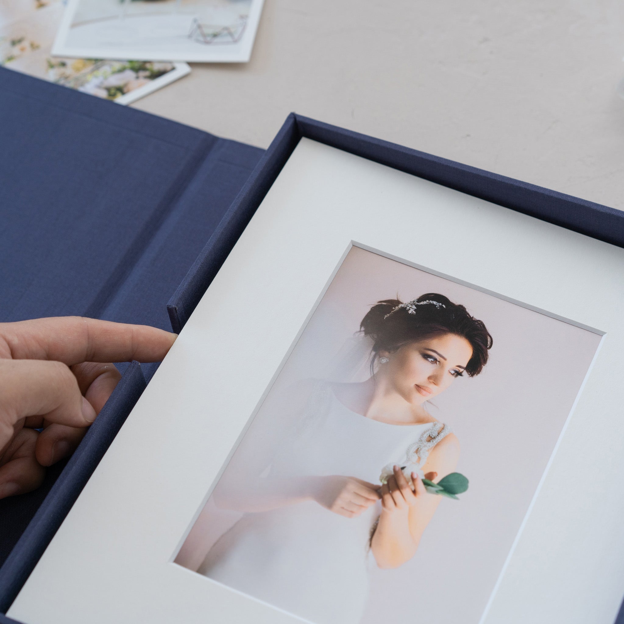 A hand is holding a framed photograph of a woman in a white dress, with a blue folder visible in the background.