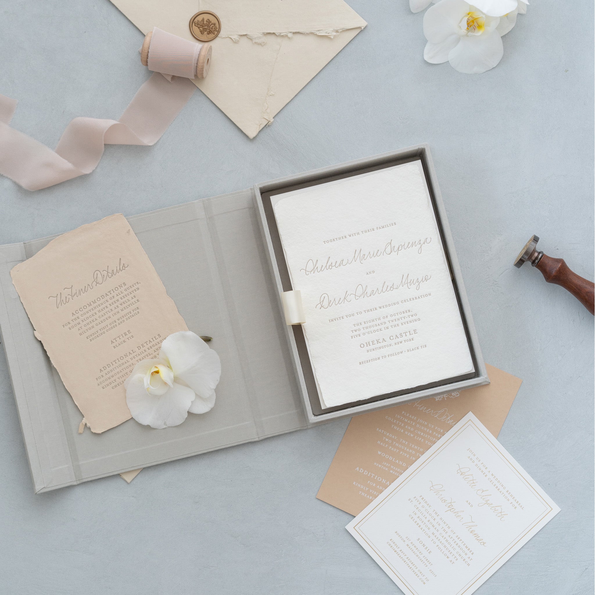 a wedding invitation with a white background and elegant cursive text, accompanied by a small envelope, a ribbon, and a flower.