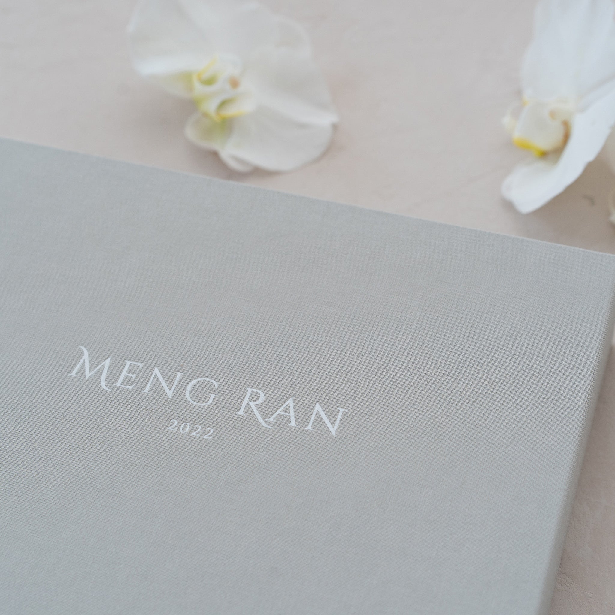 A gray box with the text "Meng Ran" and the year "2022" printed on it, along with a small white flower on the side.