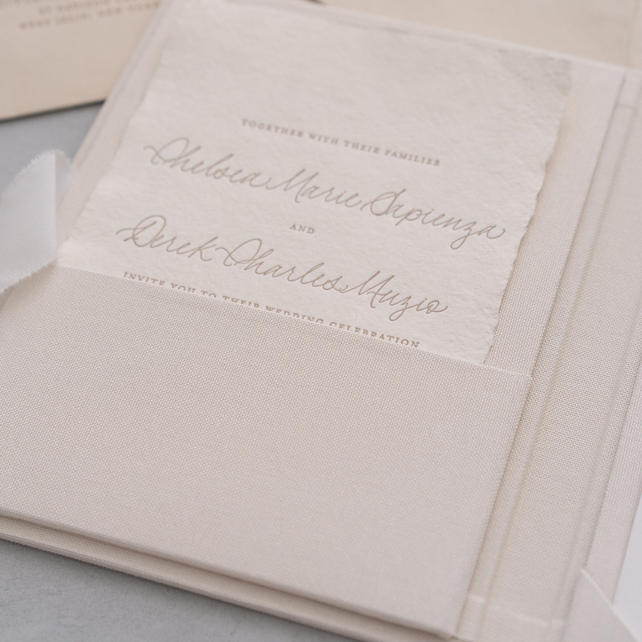 A close-up of a wedding invitation card with elegant cursive text, featuring the names of the couple and the names of their families.