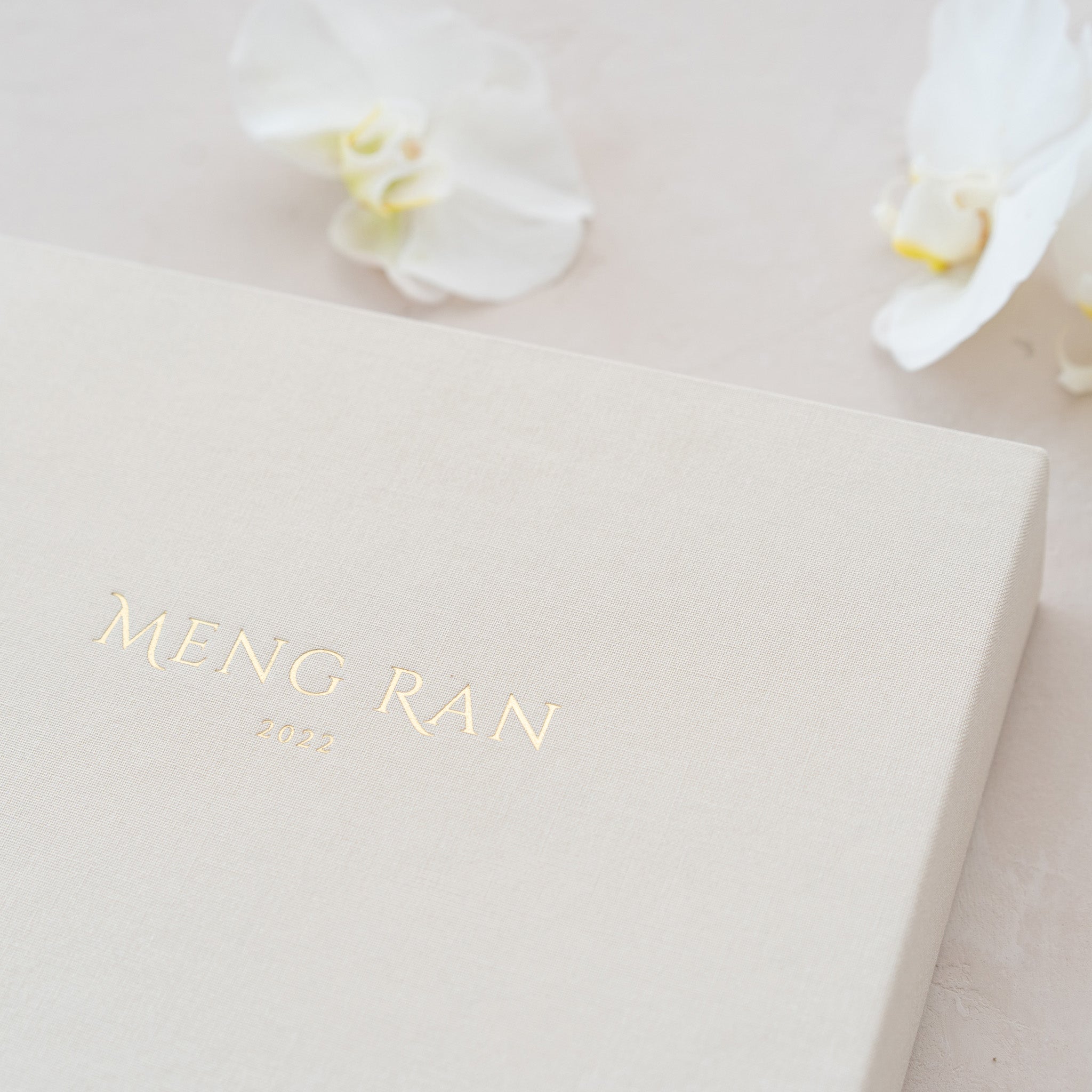 A close-up image of a white box with the text "Meng Ran" and the year "2020" printed on it, along with a small white flower in the background.