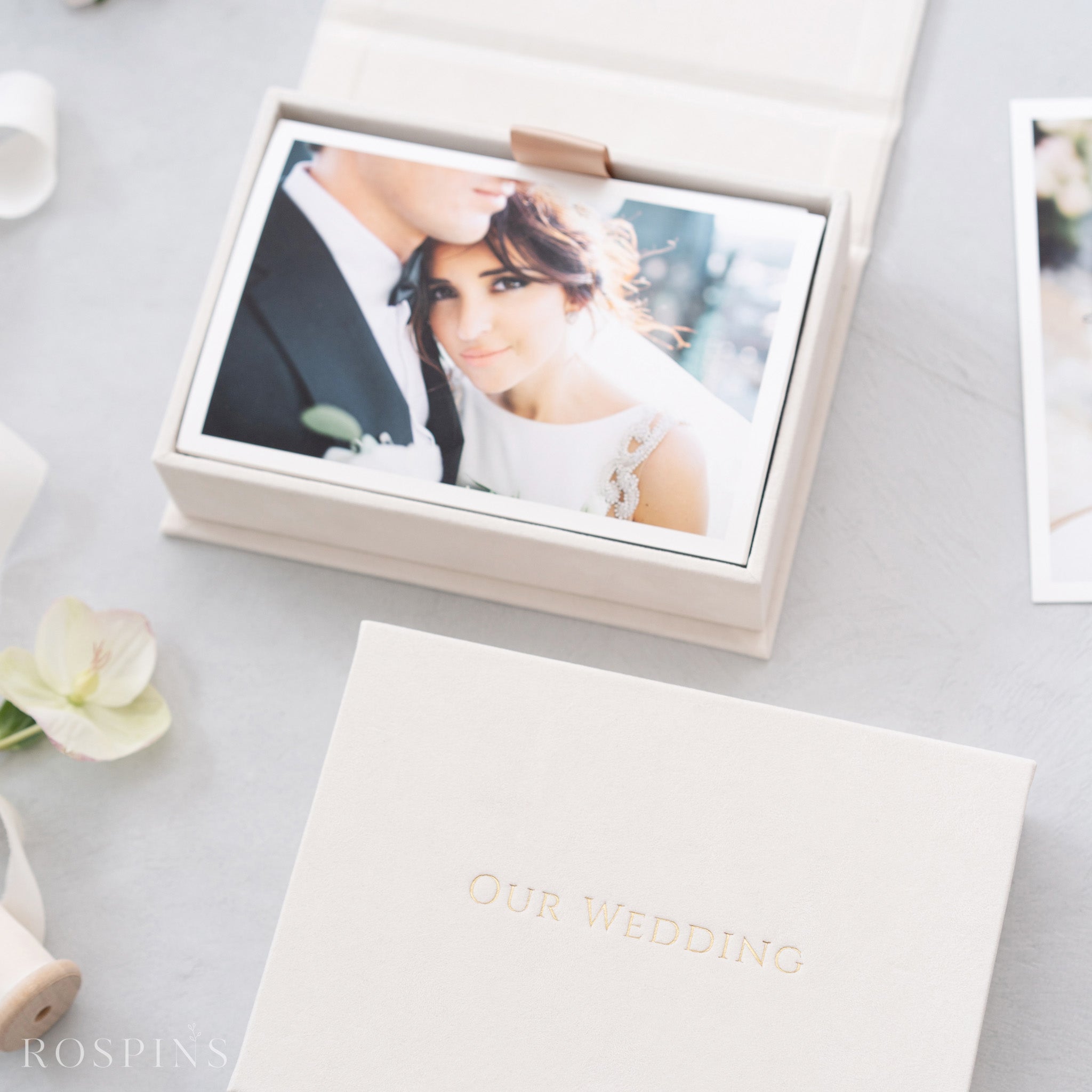 A white wedding album box with a photograph of a bride and groom inside, placed on a light-colored surface.